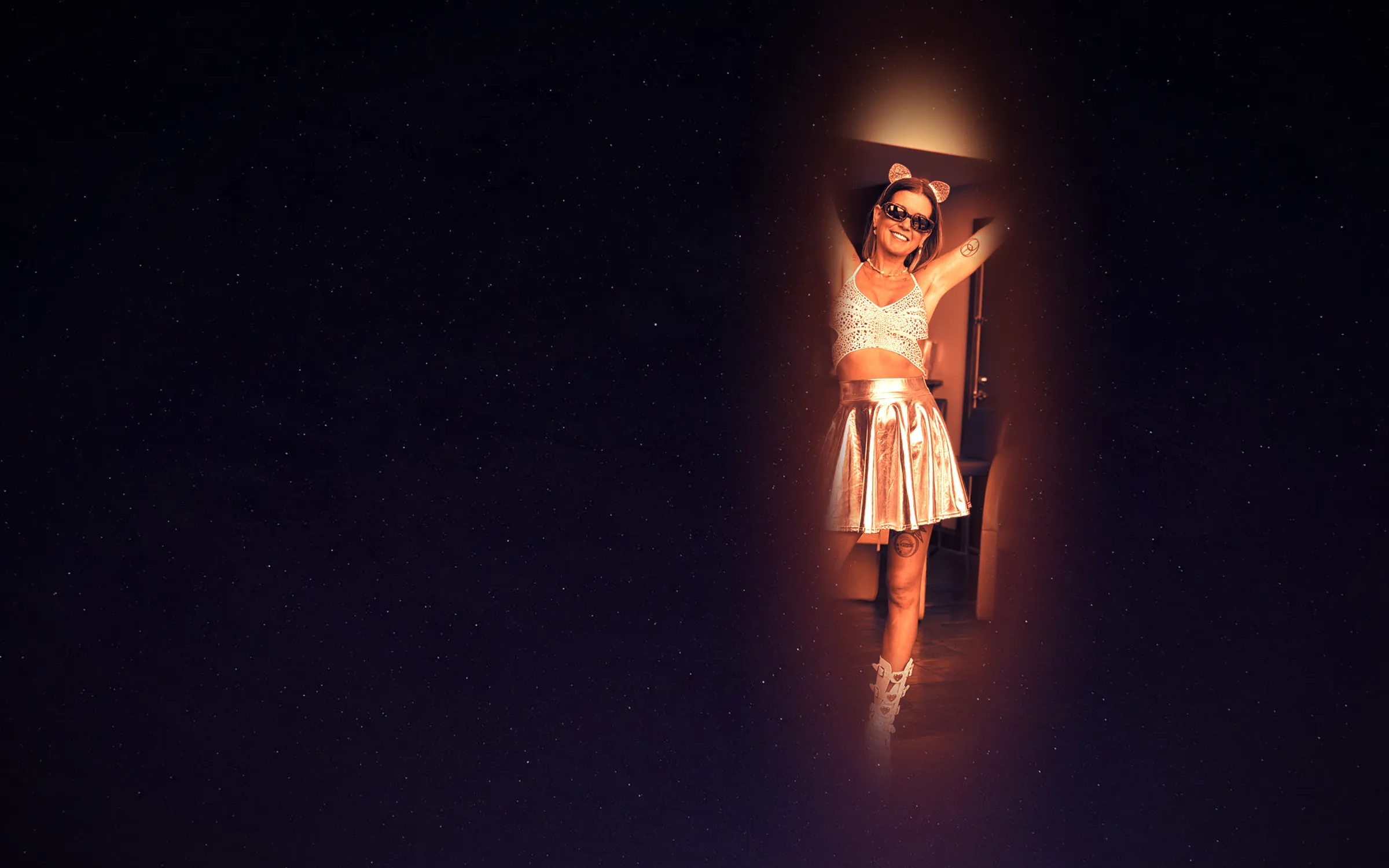 Cortnie Kairos with both arms raised, lit warm against a field of stars